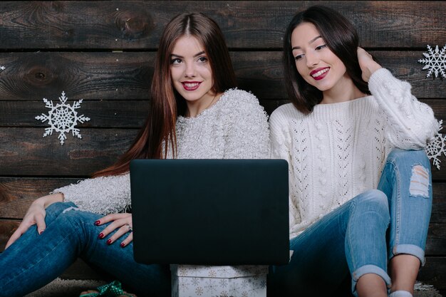 Zwei schöne Frauen, die mit einem Laptop auf dem Boden sitzen