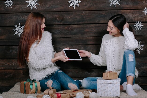 Zwei schöne Frauen sitzen auf dem Boden mit einer Tafel, zwischen Geschenken für Weihnachten