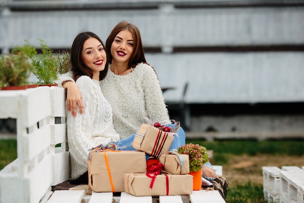 Zwei schöne frauen sitzen auf einer bank, halten geschenke in ihren händen und schauen