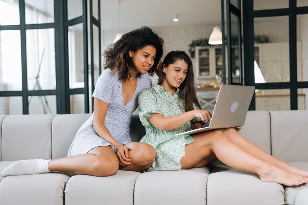 Zwei schöne junge Frauen entspannen sich auf dem Wohnzimmerboden und schauen auf einen Laptop