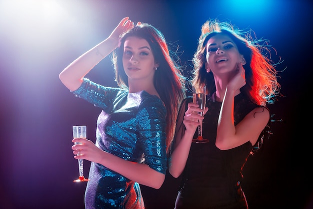 Zwei schöne Mädchen tanzen auf der Party Champagner trinkend