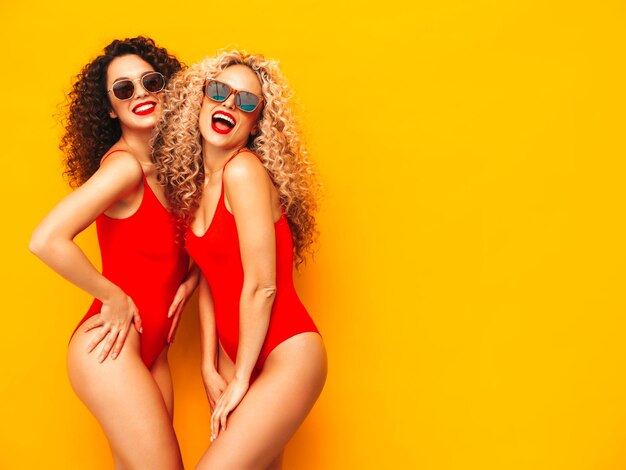 Zwei schöne sexy lächelnde Hipster-Frauen in roten Sommer-Badebekleidungs-Badeanzügen Trendige Modelle mit Afro-Locken-Frisur, die Spaß im Studio haben