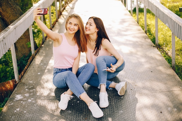 zwei schöne und helle Freunde in den rosa T-Shirts und in den Blue Jeans, die im sonnigen Park sitzen