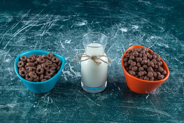 Zwei Schüssel Maisringe neben einem Glas Milch, auf blauem Hintergrund. Foto in hoher Qualität