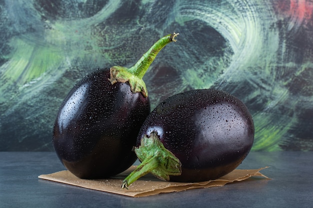 Zwei schwarze Auberginen mit Wassertropfen auf Steinhintergrund.