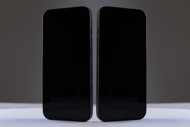 Zwei schwarze rechteckige smartphones mit glänzenden bildschirmen nebeneinander auf grau isoliert