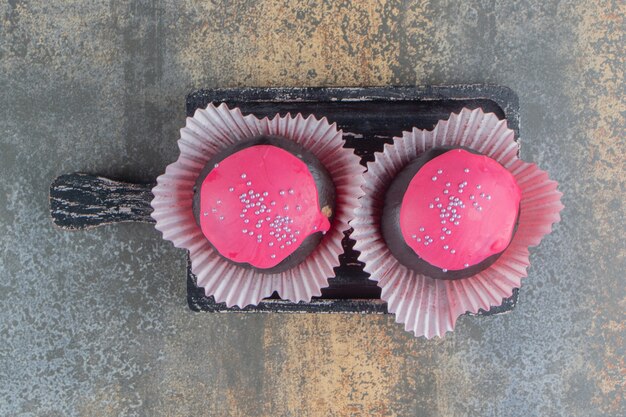 Zwei süße schokoladenkrapfen mit rosa zuckerguss und streuseln