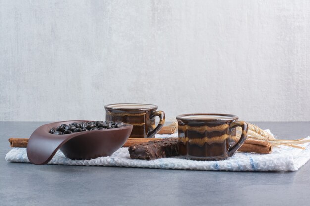 Zwei Tassen Kaffee mit Blatt Papier und Pralinen auf Tischdecke.