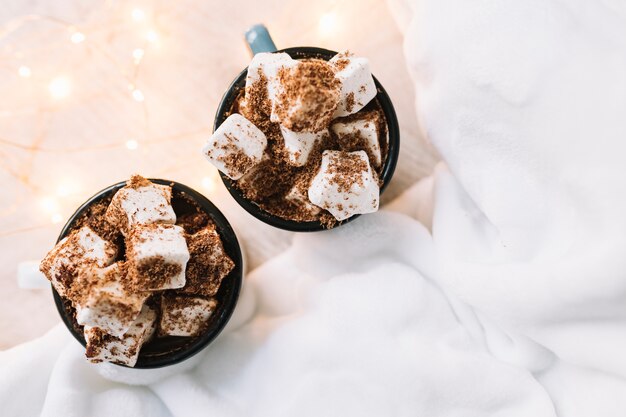 Zwei Tassen mit Marshmallows und Kakaopulver auf dem Tisch