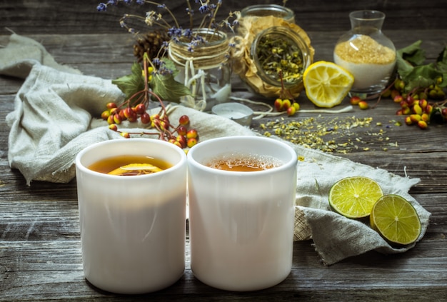 zwei Tassen Tee auf einem schönen hölzernen Hintergrund mit Zitrone und Kräutern, Winter, Herbst