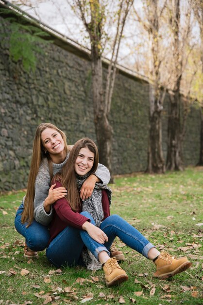 Zwei umarmende junge Frauen, die im Park sitzen