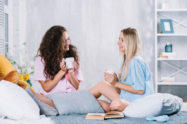 Zwei weiblicher Freund, der Tasse Kaffee auf Bett isst