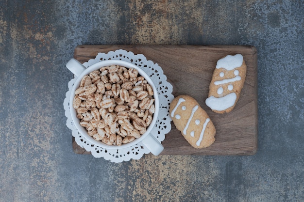 Zwei Weihnachtsplätzchen und eine Schüssel mit süßen Erdnüssen auf Holzbrett. Hochwertiges Foto