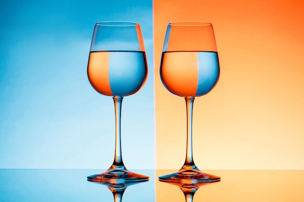Zwei Weingläser mit Wasser über blauem und orange Hintergrund.
