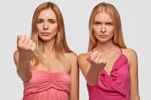 Zwei wütende blonde weibliche Stretchfäuste, warnt Sie, tragen rosa Kleider, sind unzufrieden, gestikulieren wütend