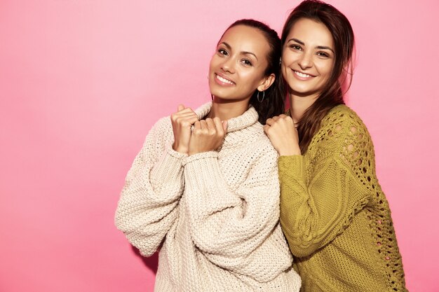Zwei wunderschöne lächelnde wunderschöne Frauen. Frauen, die in den stilvollen weißen und grünen Strickjacken, auf rosa Wand stehen.