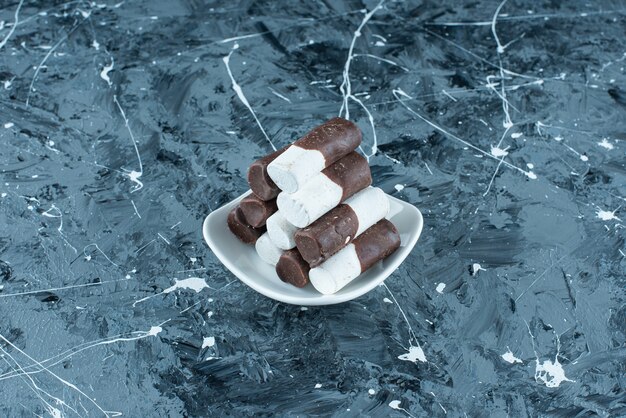 Zweifarbige Bonbons auf einem Teller auf dem blauen Tisch.