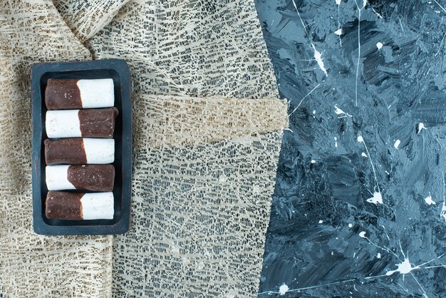 Zweifarbige bonbons auf einer holzplatte auf einer tischdecke, auf dem blauen tisch.