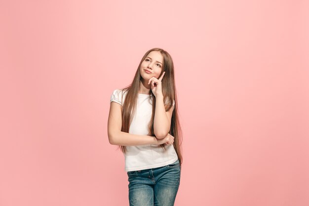 Zweifel Konzept. Zweifelhaftes, nachdenkliches jugendlich Mädchen, das sich an etwas erinnert. Menschliche Emotionen, Gesichtsausdruckkonzept. Teenager, der im Studio auf rosa Hintergrund aufwirft