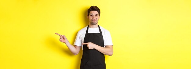 Zweifelhafter Barista in schwarzer Schürze, der mit den Fingern nach rechts zeigt und skeptisch und unamüsiert übersteht