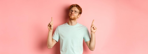 Kostenloses Foto zweifelhafter rothaariger typ mit brille, der die stirn runzelt und mit den fingern auf etwas enttäuschtes zeigt