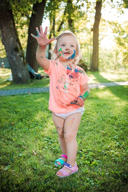 Zweijähriges Mädchen in Farben gegen grünen Rasen befleckt