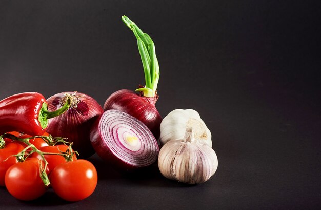 Zwiebel und Knoblauch und Peperoni und Tomaten isoliert auf einem schwarzen.