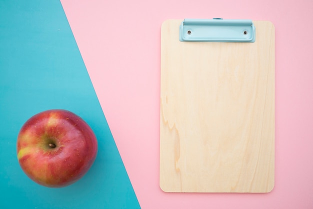 Kostenloses Foto zwischenablage und apfel auf blauem und rosa hintergrund