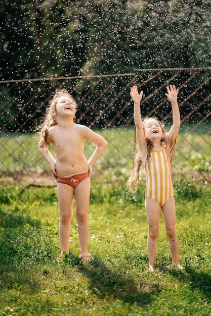 01032022 Bar Ucrania dos hermanitas vestidas con trajes de baño están salpicando agua en un día soleado de verano en el patio de la casa sobre un fondo verde