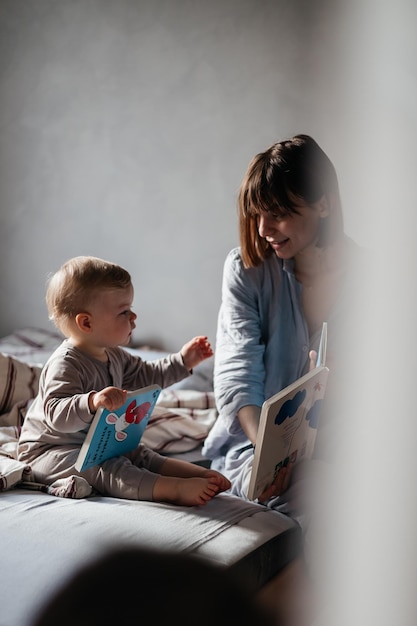 02032022 Vinnitsa Ukraine Junge Mutter und kleine Tochter wachten im Bett auf und hatten Spaß beim Umarmen, als sie ein Buch ansahen