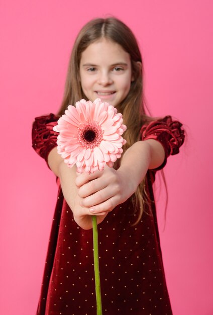 1 Mädchen Teenager in einem roten Kleid mit einer Gerbera-Blume auf einer rosa Oberfläche