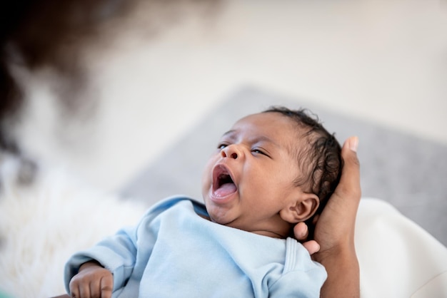 1 Monat altes afroamerikanisches Neugeborenes gähnt schläfrig, während es auf der Handfläche seiner Mutter liegt