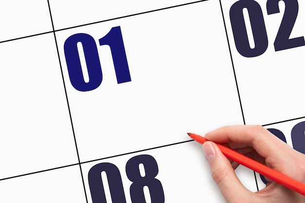 1. Tag des Monats Die Hand, die den roten Stift hält, zeigt auf ein leeres Kalenderdatum