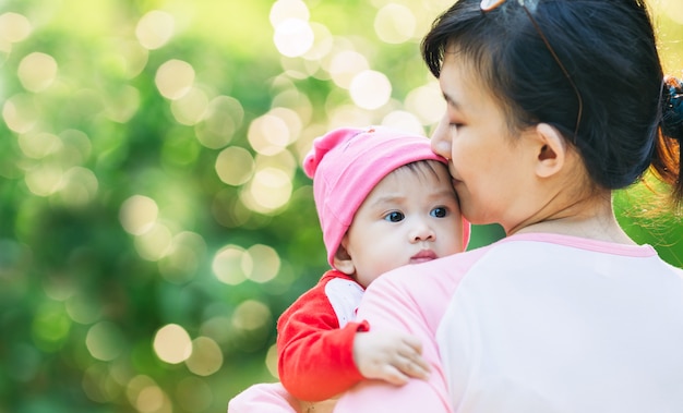 10 Monate nettes Baby, das glücklich sich fühlt und mit ihrer Mutter im Garten lächelt.