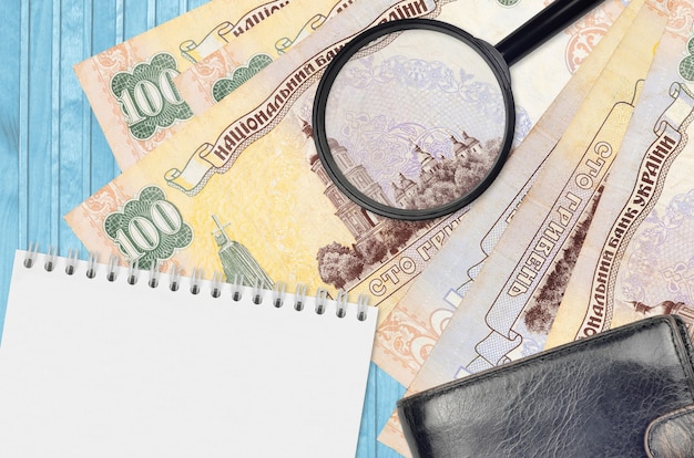 100 ukrainische Griwna-Scheine und Lupe mit schwarzer Geldbörse und Notizblock