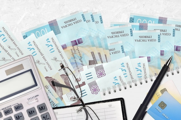 1000 billetes de hryvnias ucranianas y calculadora con gafas y bolígrafo. Concepto de temporada de pago de impuestos o soluciones de inversión. Planificación financiera o papeleo contable