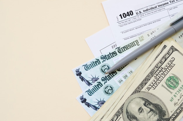 1040 Formular zur individuellen Einkommensteuererklärung mit Rückerstattungsscheck und Hundert-Dollar-Scheinen auf beigem Hintergrund