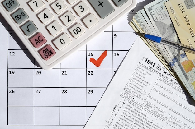 1041 Declaración de impuestos sobre la renta para sucesiones y fideicomisos en blanco con calculadora de billetes de dólar y bolígrafo en la página del calendario con el 15 de abril marcado