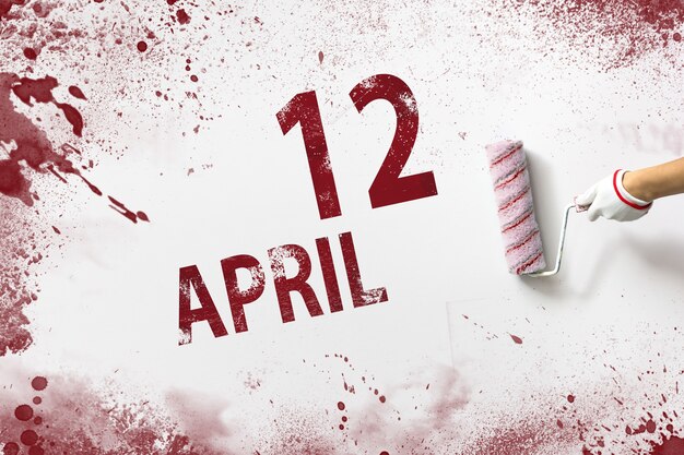 12. April. Tag 12 des Monats, Kalenderdatum. Die Hand hält eine Rolle mit roter Farbe und schreibt ein Kalenderdatum auf einen weißen Hintergrund. Frühlingsmonat, Tag des Jahreskonzepts.