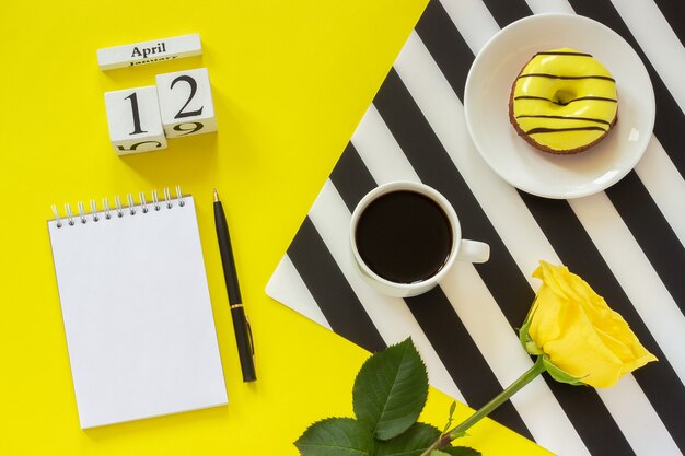 12 de abril. Bloco de notas cor-de-rosa da rosquinha da xícara de café no fundo amarelo. Local de trabalho elegante conceito