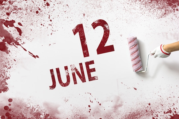 12 de junho. Dia 12 do mês, data do calendário. A mão segura um rolo com tinta vermelha e escreve uma data do calendário em um fundo branco. Mês de verão, dia do conceito de ano.