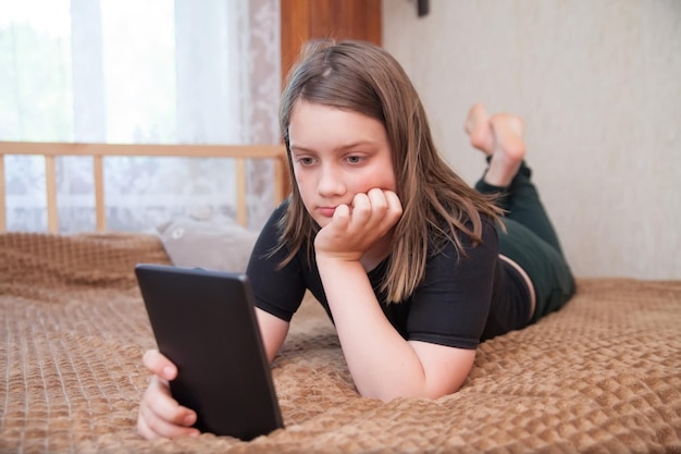 12-jähriges Mädchen, das mit E-Book auf dem Bett liegt und liest