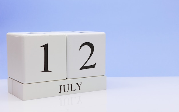 12 de julio. Día 12 del mes, calendario diario en mesa blanca con reflejo, con fondo azul claro.