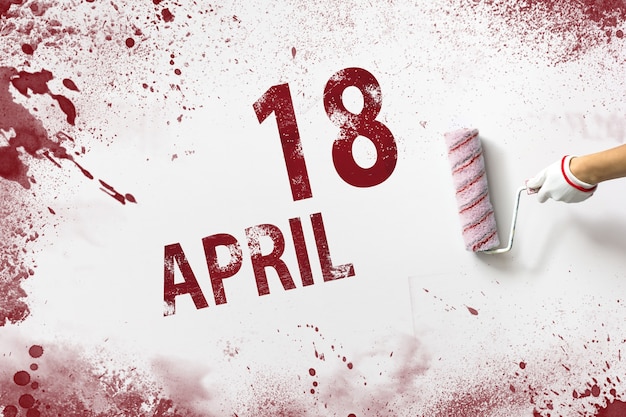 18. April. Tag 18 des Monats, Kalenderdatum. Die Hand hält eine Rolle mit roter Farbe und schreibt ein Kalenderdatum auf einen weißen Hintergrund. Frühlingsmonat, Tag des Jahreskonzepts.