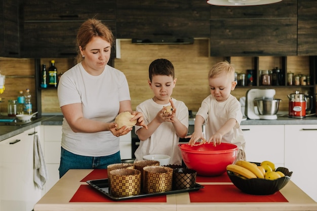 18112018 Vinnitsa Ucrania mamá con niños amasa la masa para deliciosos pasteles que preparan en la cocina en casa
