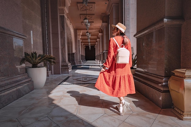 19. Januar 2025 Abu Dhabi Vereinigte Arabische Emirate Junge Touristin mit rotem Kleid und Strohhut geht in einem Luxushotel und genießt ihren Urlaub