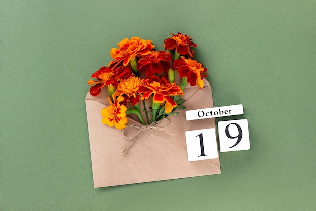 Foto 19 de octubre ramo de flor de naranja en sobre artesanal y fecha de calendario sobre fondo verde concepto mínimo hola plantilla de otoño para su tarjeta de felicitación de diseño