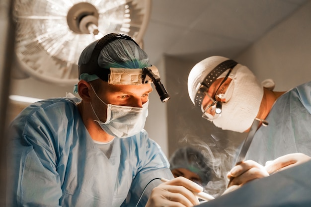 2 cirujanos con faro hacen operación plástica en clínica médica. Cirugía plástica de aumento de pecho y corrección en clínica médica.
