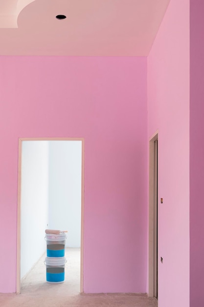 2 cubos de pintura de plástico en el marco de la puerta con una pared de cemento rosa pastel dentro del sitio de construcción de la casa