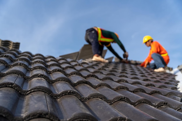 2 Dachdecker, die an der Höhenarbeit arbeiten, um die Betondachziegel auf dem neuen Dach des neuen modernen Hochbaus zu installieren Selektiver Fokus auf Betondachziegel